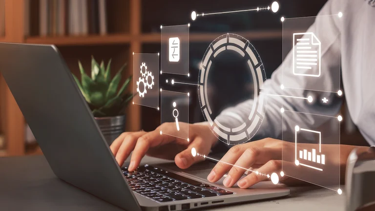 Hands typing on a laptop, with transparent icons of gears, documents and charts above the keyboard